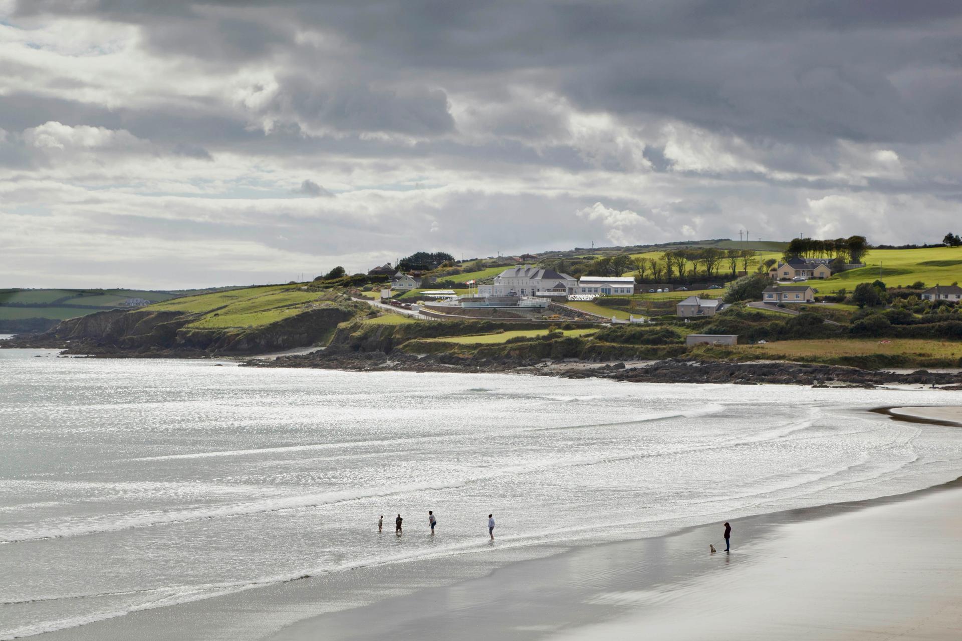Folk går längs en irländsk strand med frodig grönska i bakgrunden. 