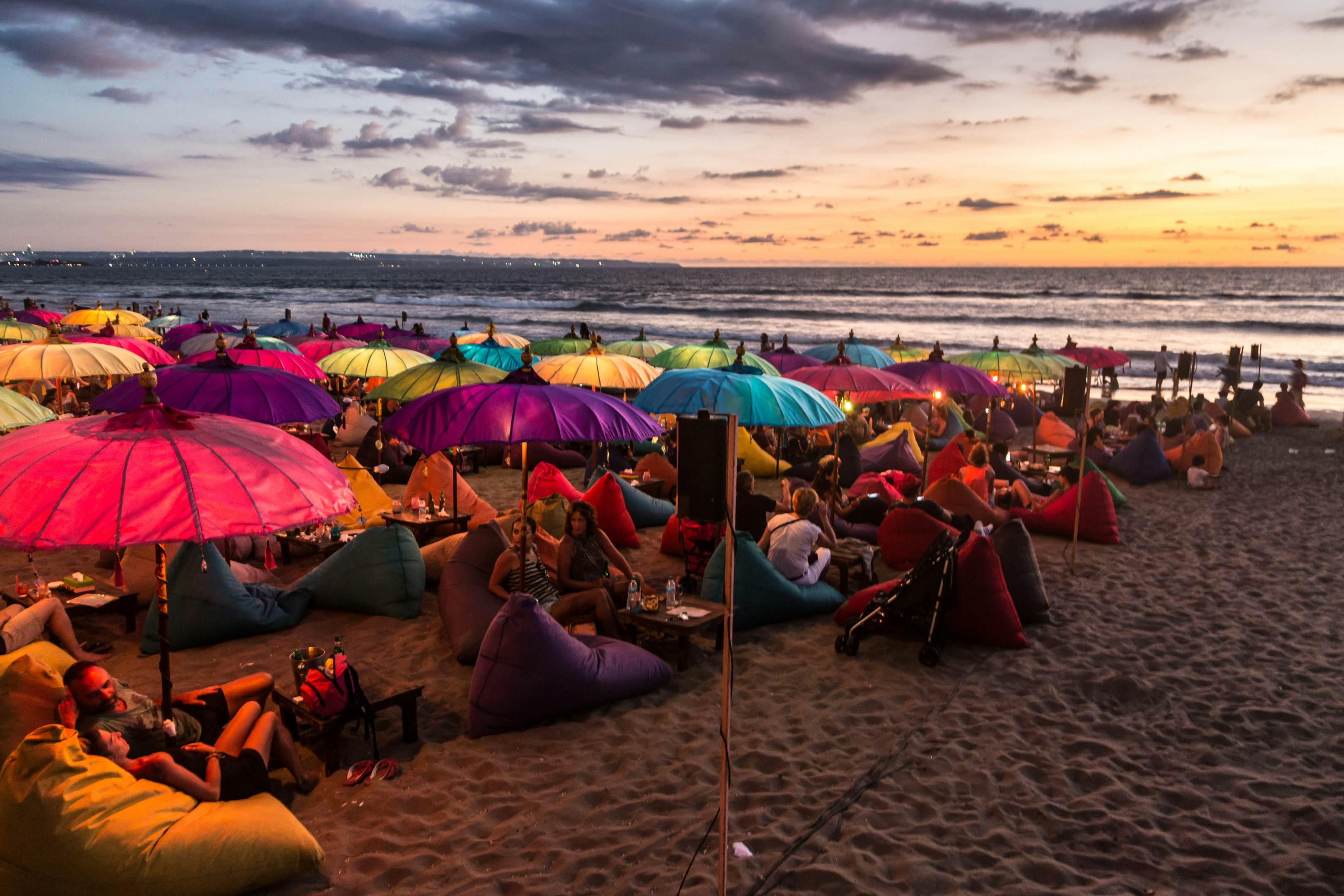 February 19, 2016: A crowd of people share food and drink under colourful umbrellas during sunset on Kuta beach.