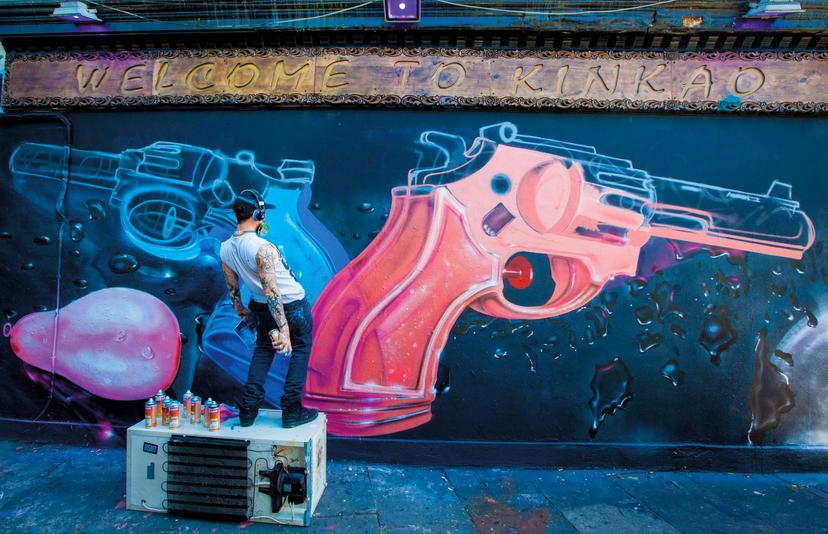 A street artist spray paints two colourful guns onto the wall of Kinkao Korean, in Shoreditch.
