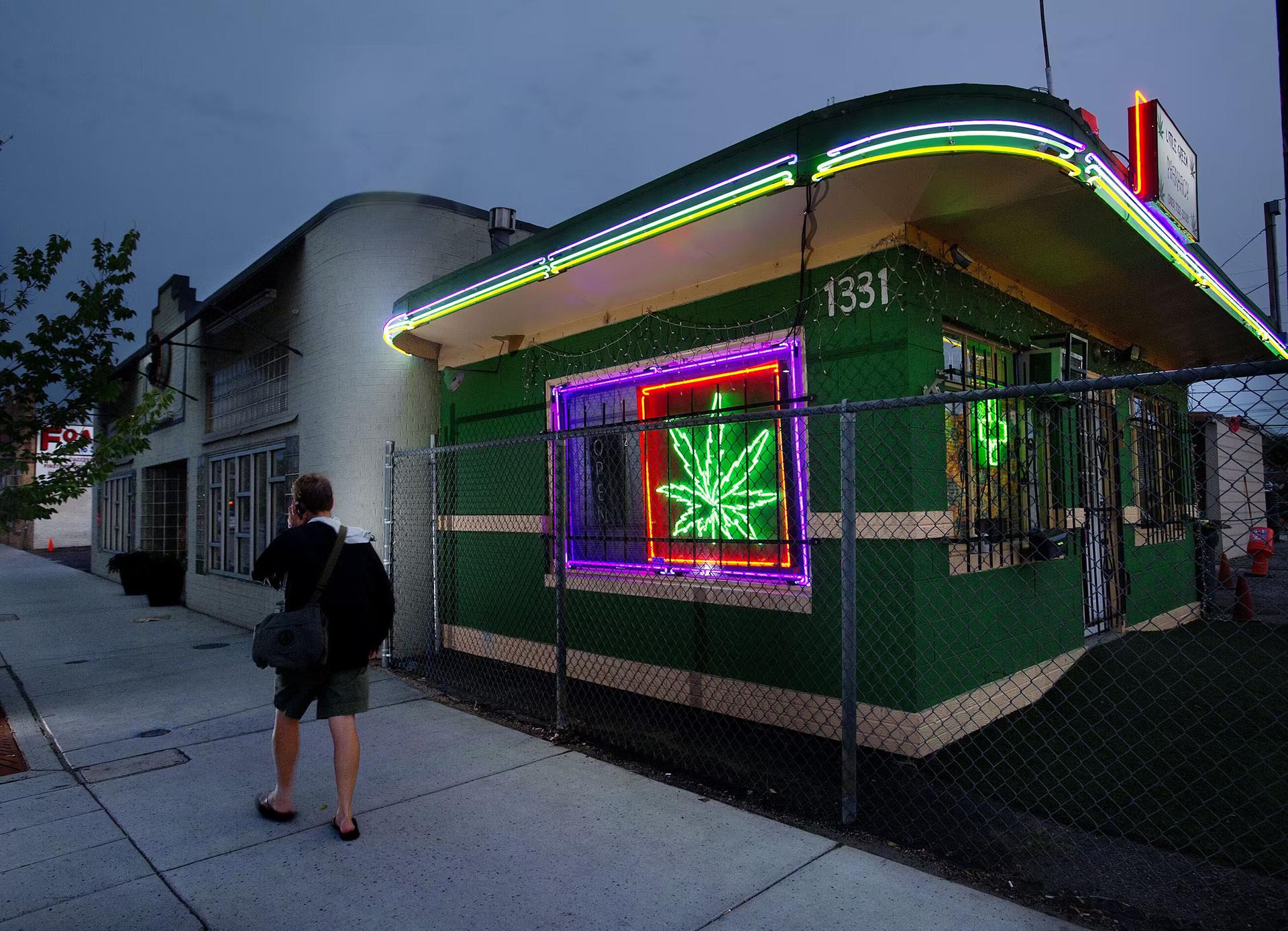 A man walks past a cannabis dispensary with a glowing pot leaf sign