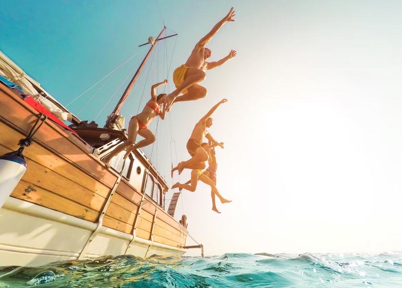 Five people jumping from a sailboat into the ocean during summer.