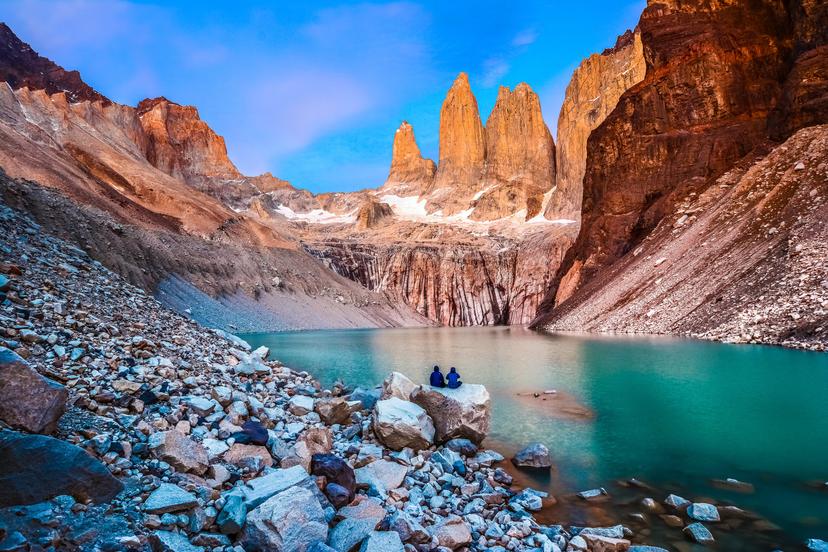 A couple sit on a rock at Laguna Torres and observe the famous three towers in dawn light.