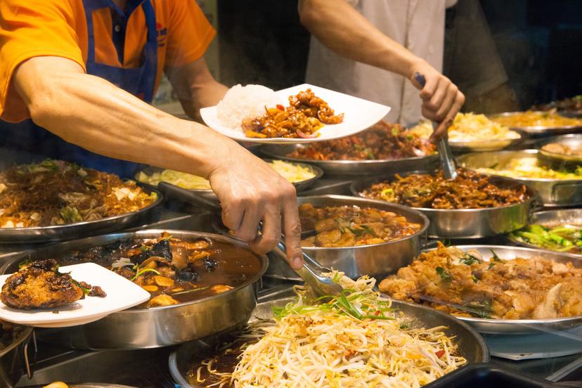 Man is putting food on the plate at one of the singaporean hawker centers.