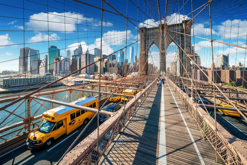 Traffic (with yellow taxis) and pedestrians cross Brooklyn Bridge on a sunny day.