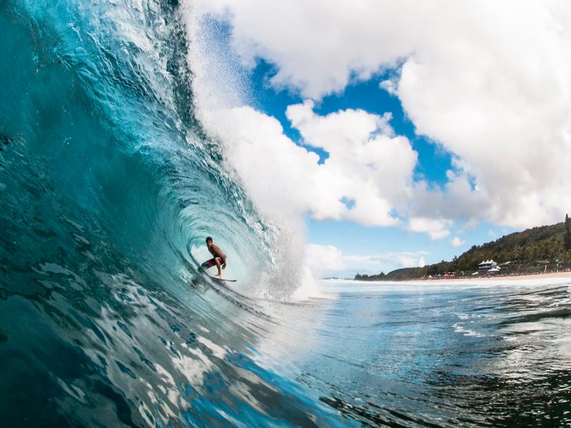 A professional surfer rides through a perfectly blue North Shore barrel