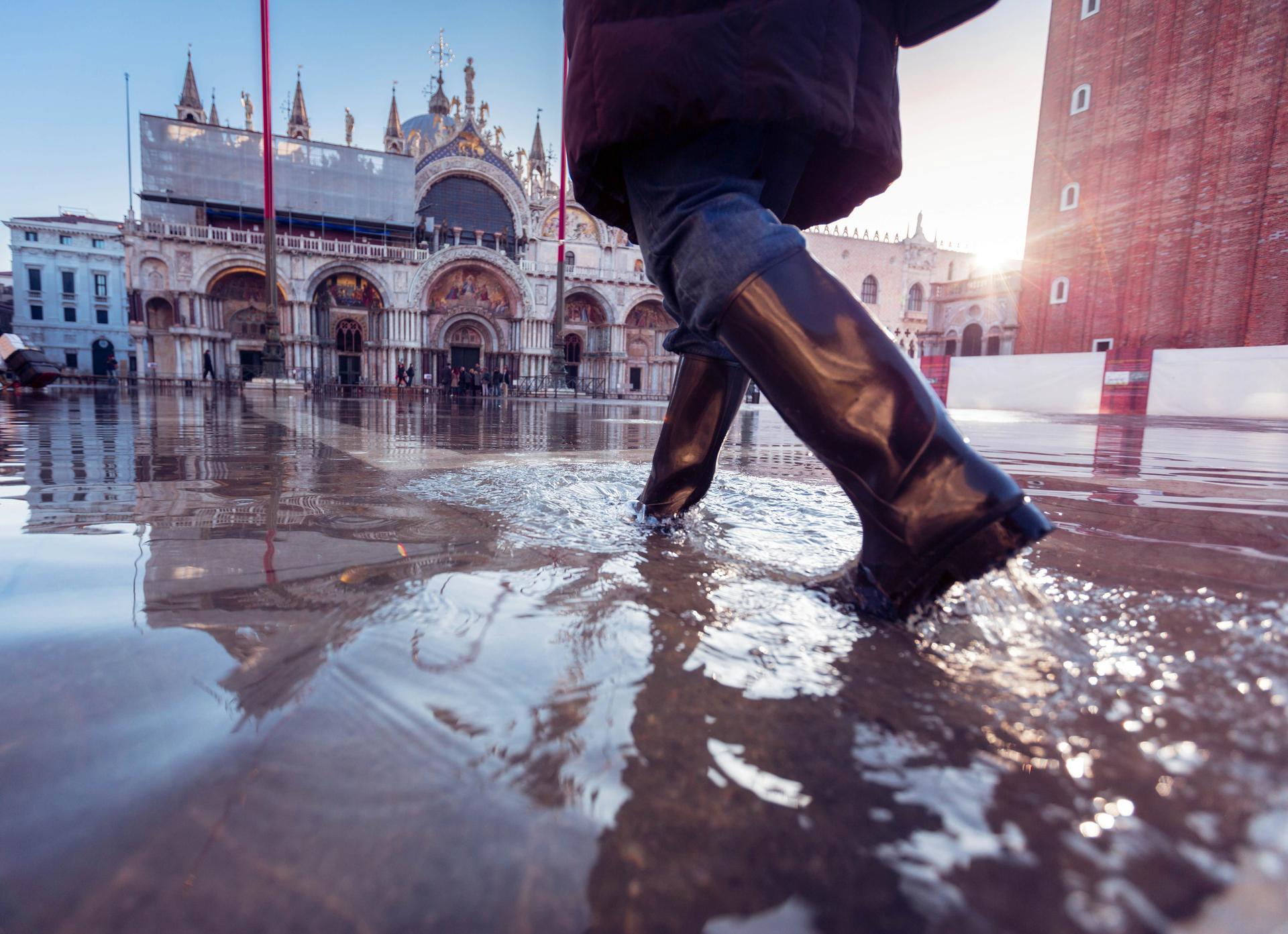 En kvinna i gummistövlar går över Markusplatsen i Venedig under acqua alta i Venedig