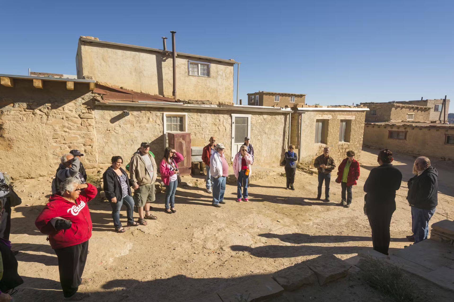 People standing in a circle outside adobe buildings at Acoma Pueblo