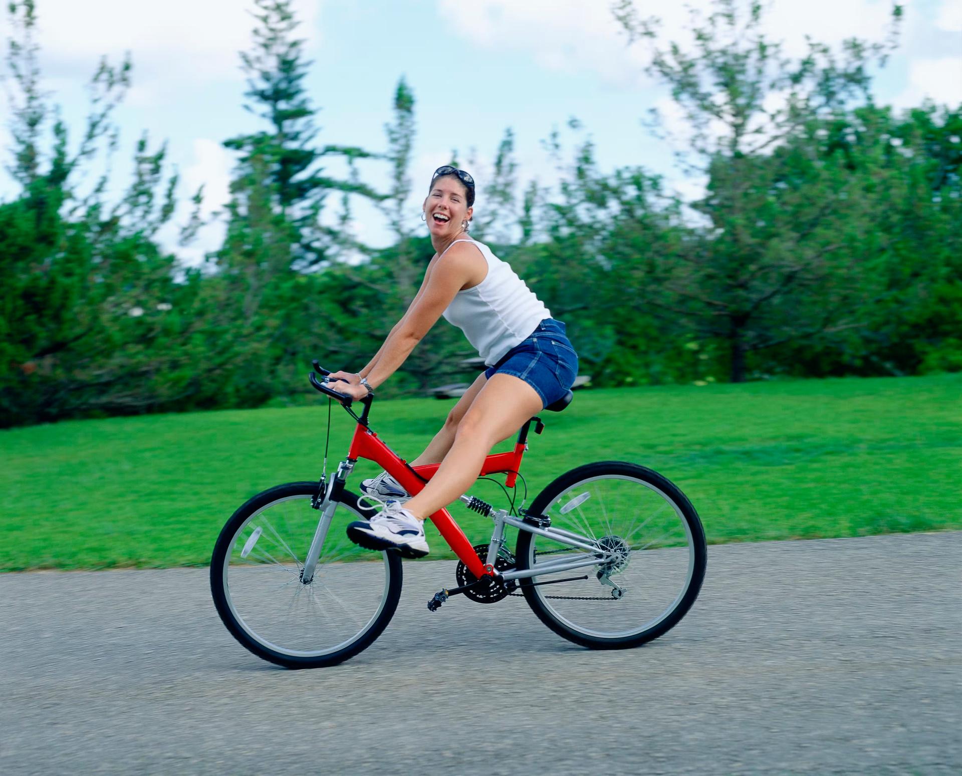 En ung kvinna sticker ut båda benen och ler mot kameran när hon cyklar.