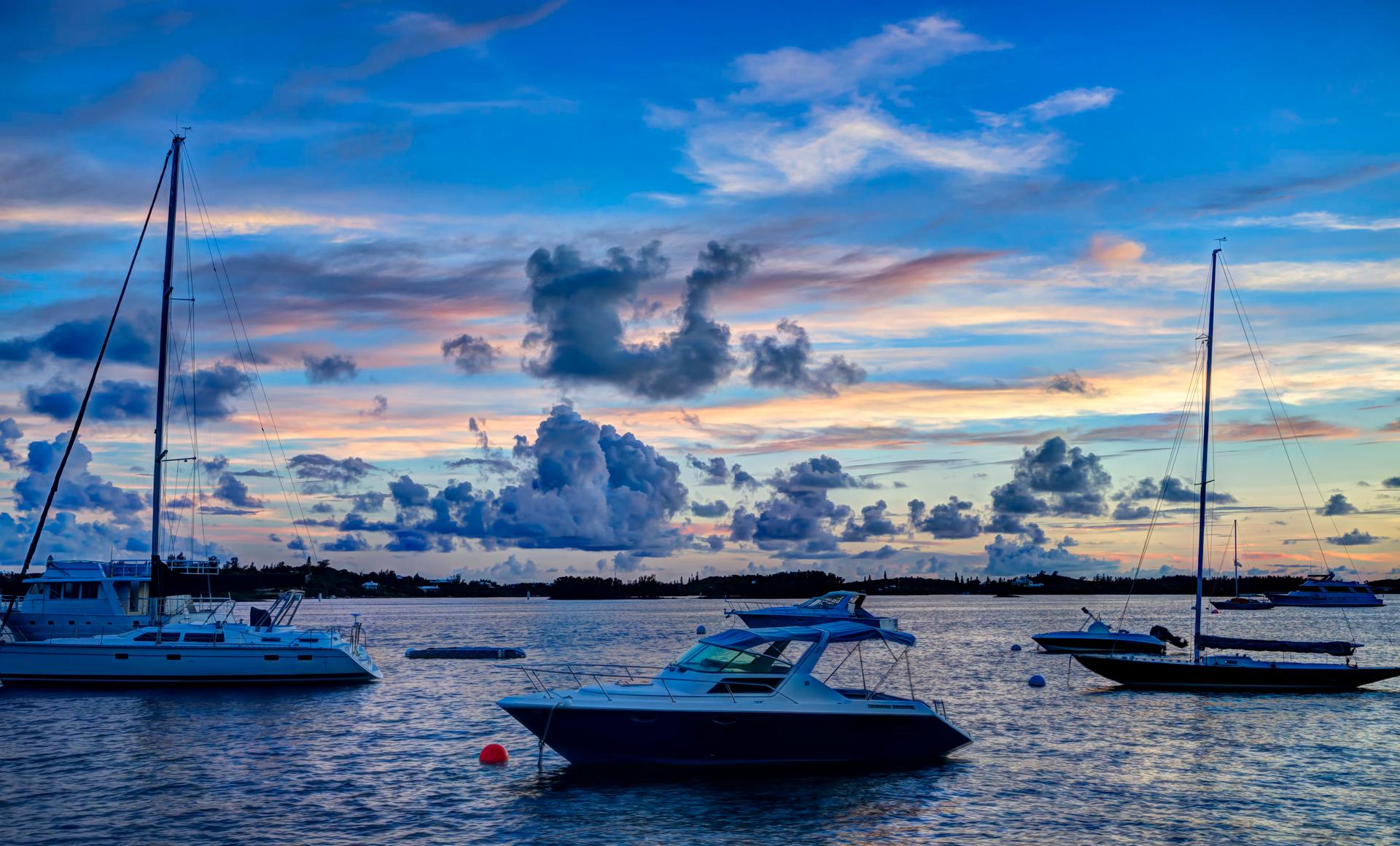 En trio båtar förtöjda i havet under solnedgången. 