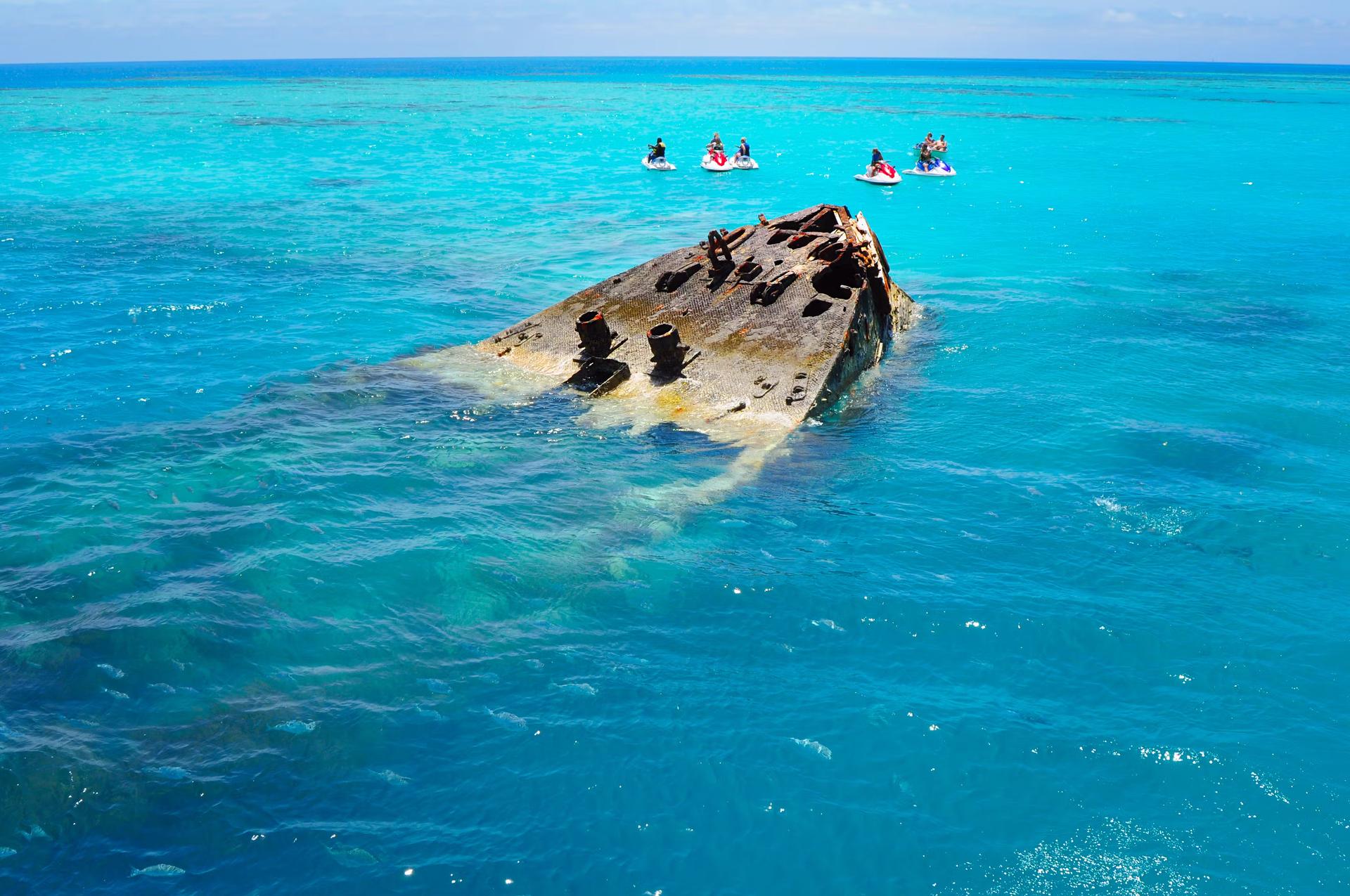En grupp människor i vattenskoter stannar bredvid ett halvt nedsänkt skeppsvrak i havet nära Bermudaön. 