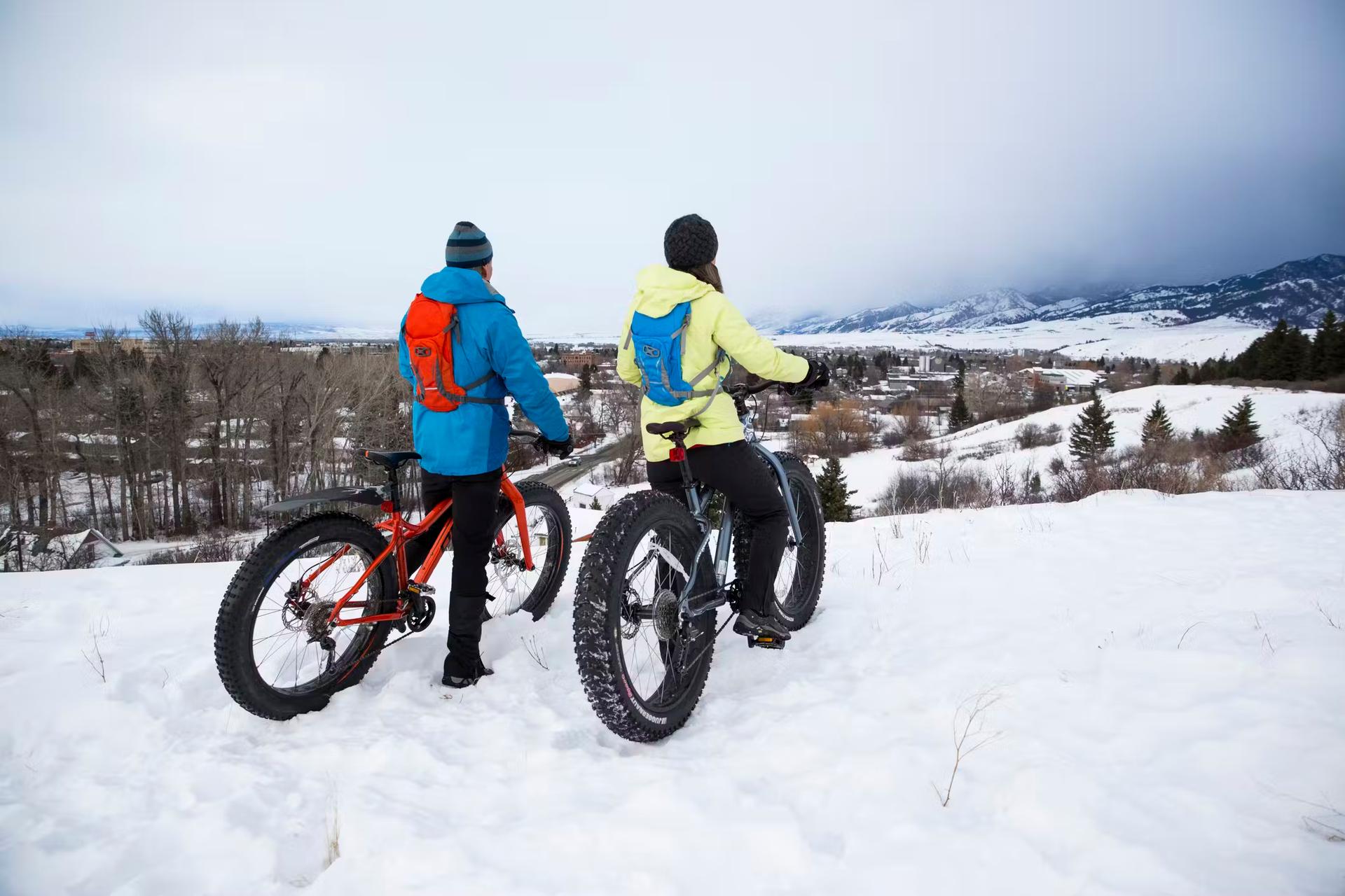 Two cyclists on fat bikes with wide tires pause to look across a snowy landscape in Montana