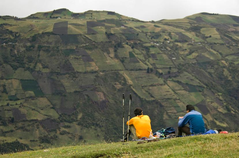Two hikers take a food break on a grassy hill in a remote valley outside of the town of Riobamba.