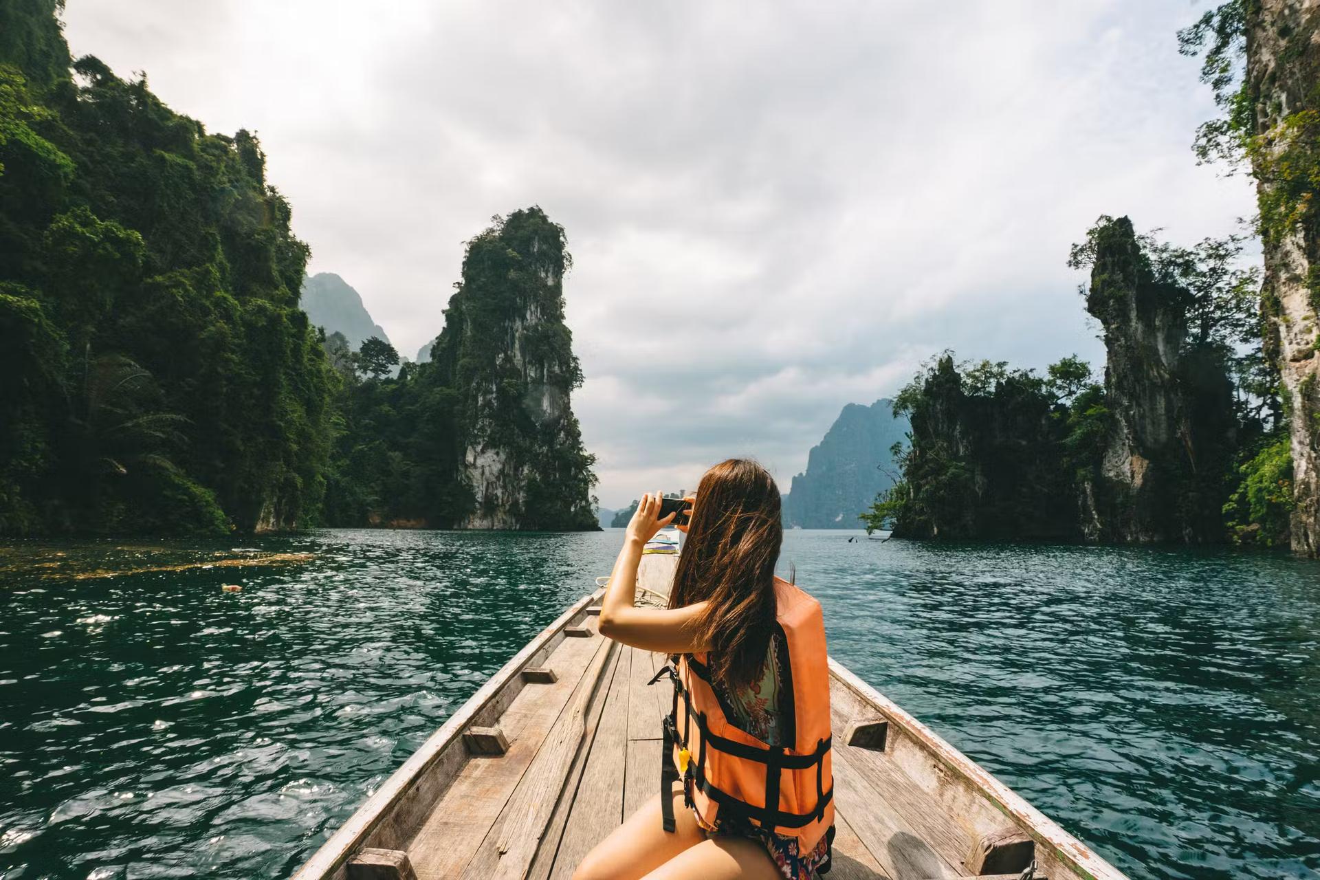 Kvinnlig turist utforskar en frodig sjö omgiven av djungel och kalkstensklippor i Khao Sok National Park