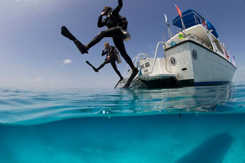 Over/under view showing divers performing giant stride entry into the clear calm waters of the Atlantic ocean.