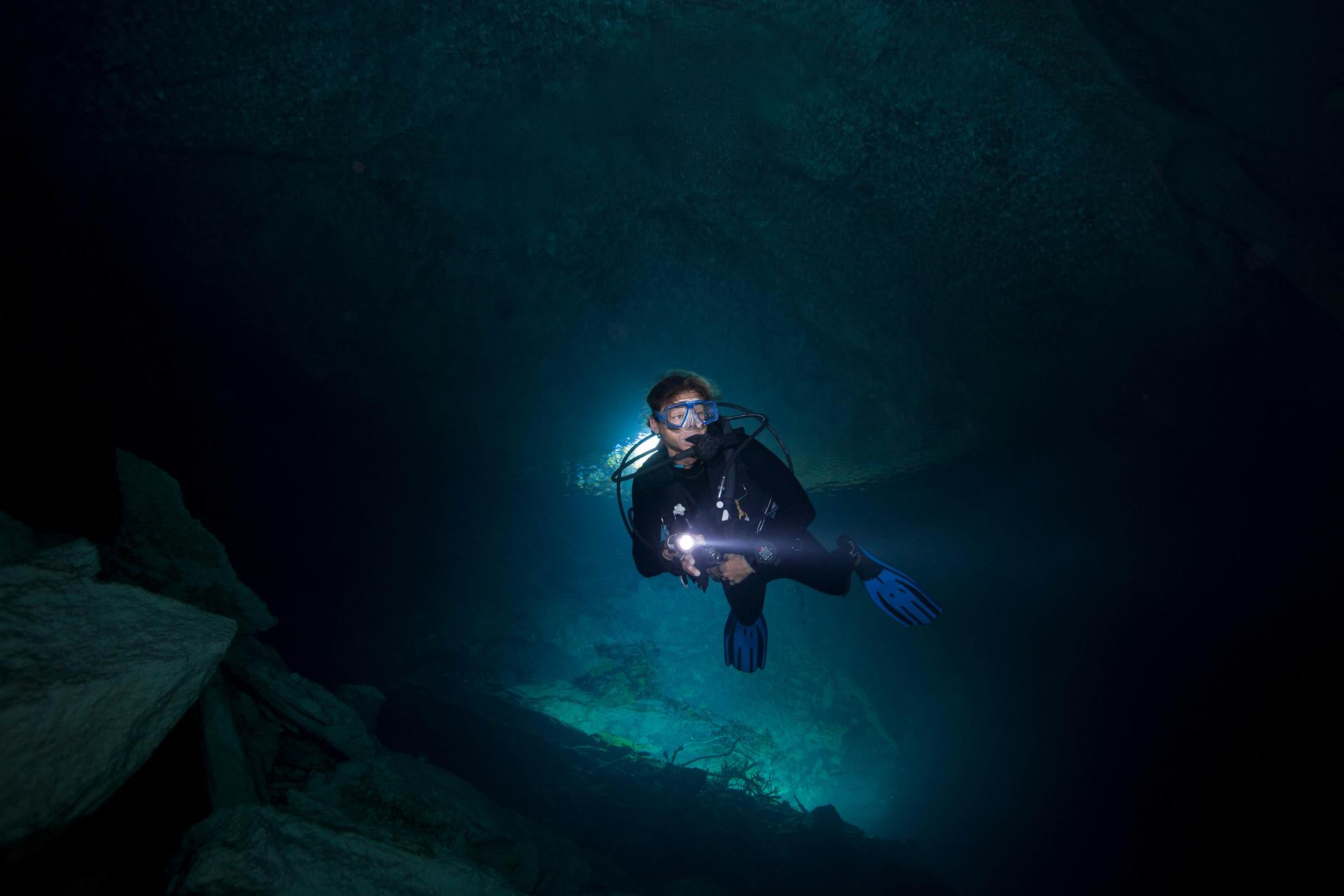 Underwater image of a scuba diver holding a large flashlight in an underwater cave in The Bahamas