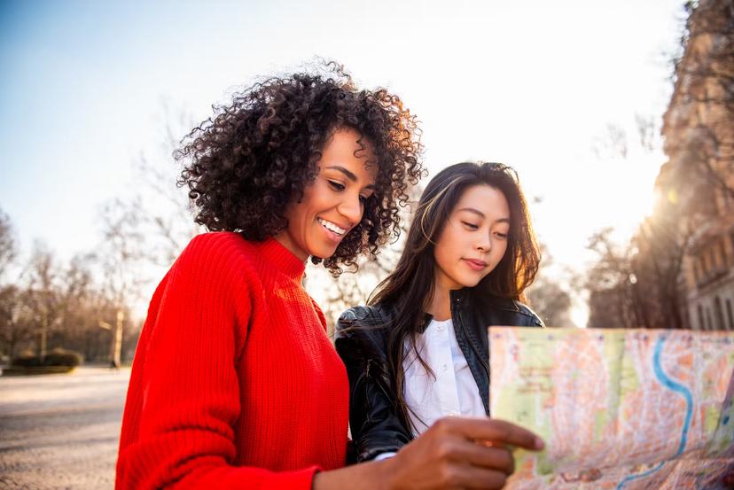 Two smiling female friends looking at a map together in Italy