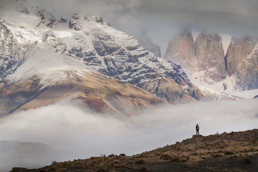 A hiker stands in awe of the huge granite peaks of the three Torres del Paine, part of the larger range of the Cordillera Paine.