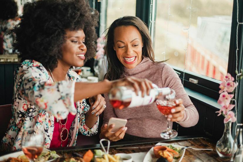 Two women are enjoying a meal in a restaurant with rose wine. They have prawns and a sharing platter in front of them.