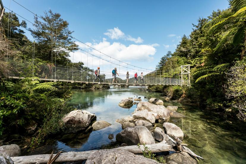 Family of five walking a rope suspension bridge across a calm lagoon