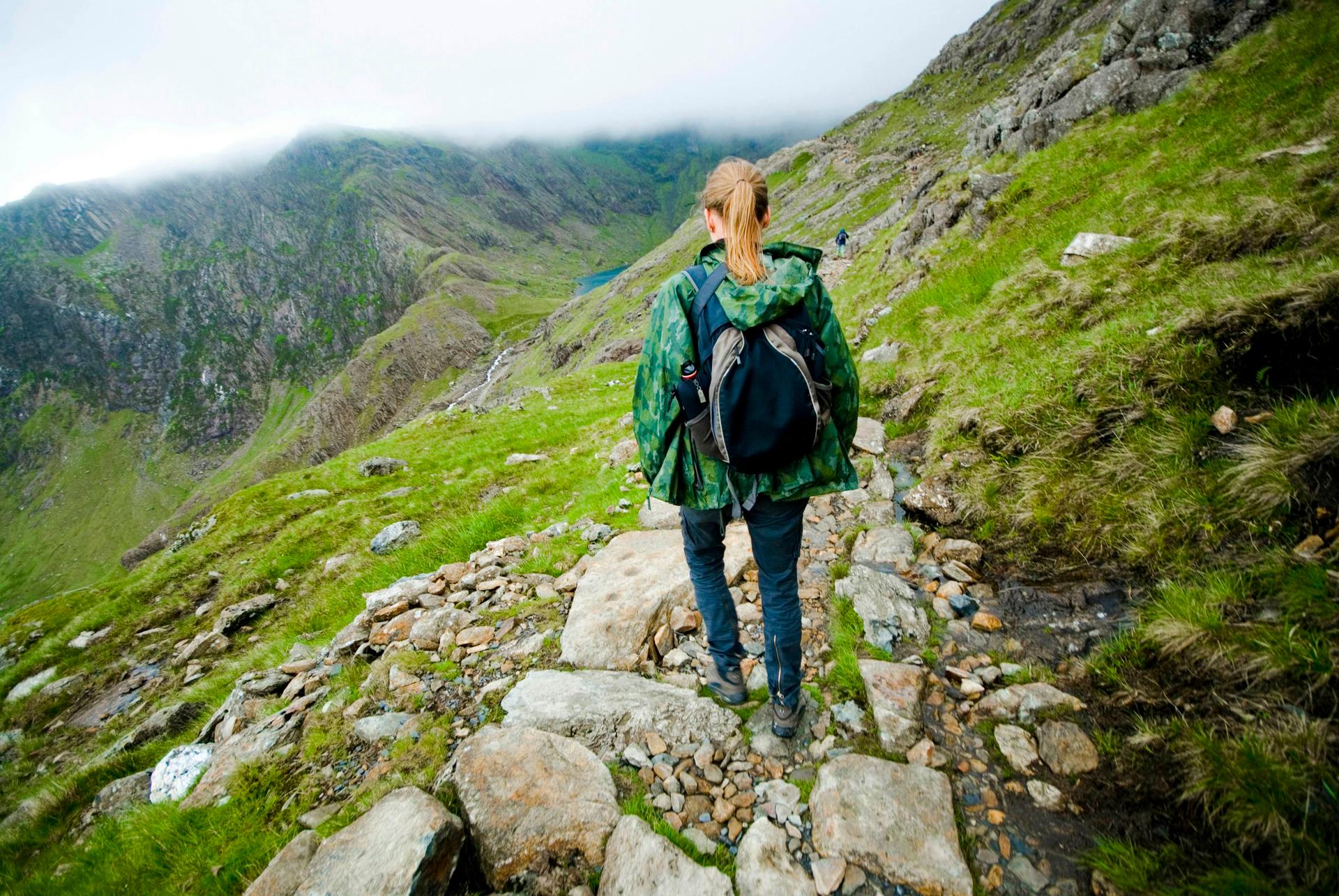 A trekker in a backpack and raincoat walks the Pyg Track on Mount Snowdon in Nant Peris, Wales, United Kingdom