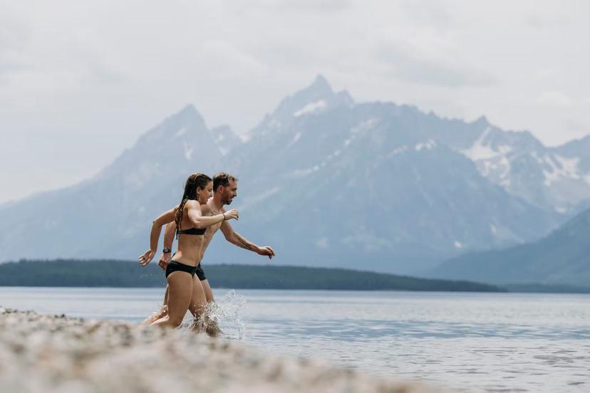 Couple runs into Jackson Lake for a swim, Tetons in the background