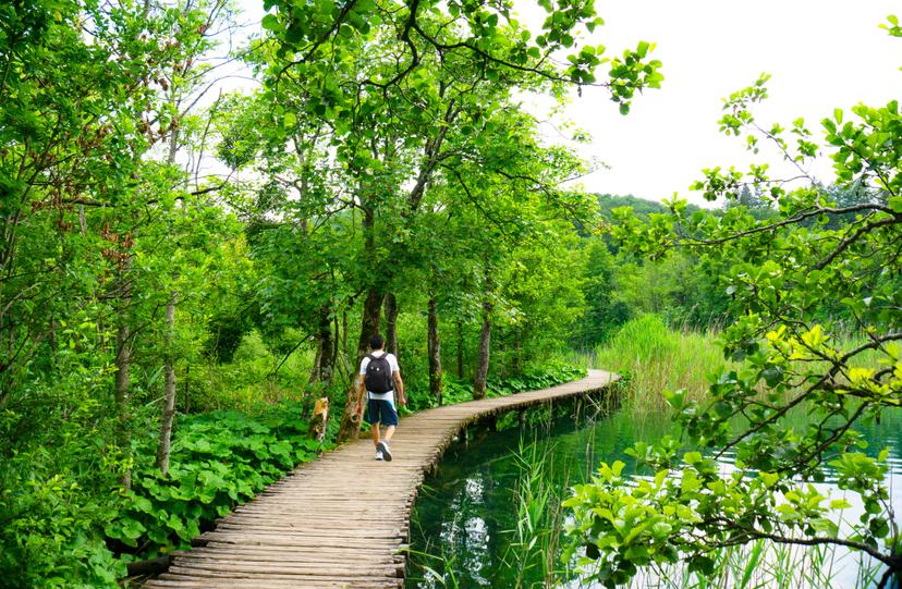 Man walking on a wooden boardwalk in the Plitvice Lakes National Park.