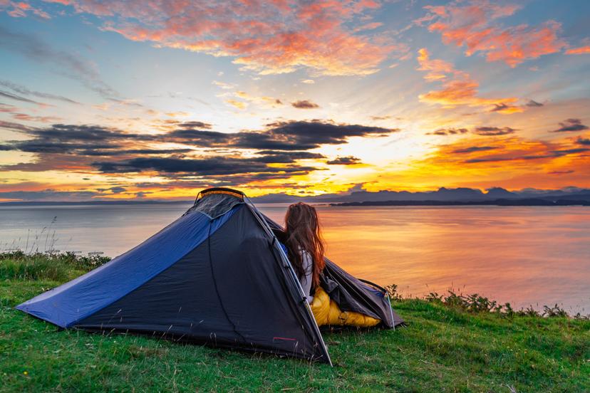 Woman watching the morning sunrise over water from her tent while wild camping in the Isle of Skye, Scotland, UK; Shutterstock ID 1822498943; your: Tasmin Waby; gl: 65050; netsuite: Online Editorial; full: Demand Project