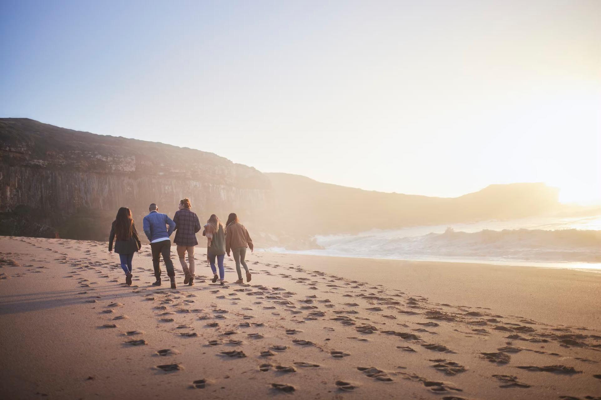 Grupp vänner som går tillsammans på stranden i solnedgången