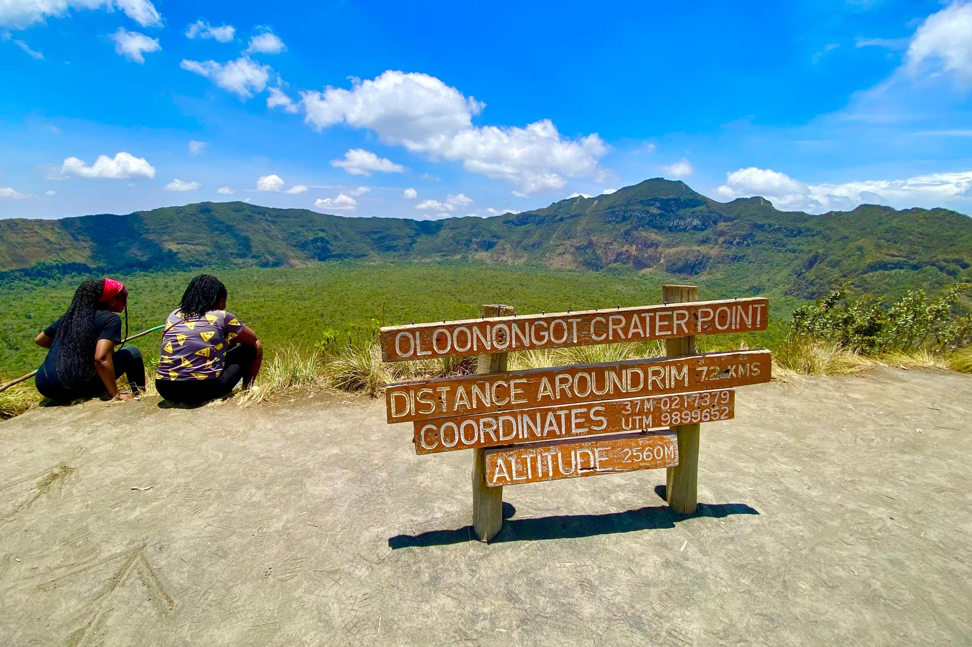 Två vandrare sitter vända mot en vulkantopp i en nationalpark