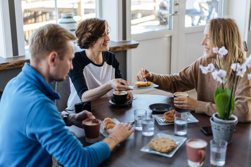 Group of cheerful women and man chatting happily while enjoying breakfast meal in cafe, Norway, Lofoten islands

