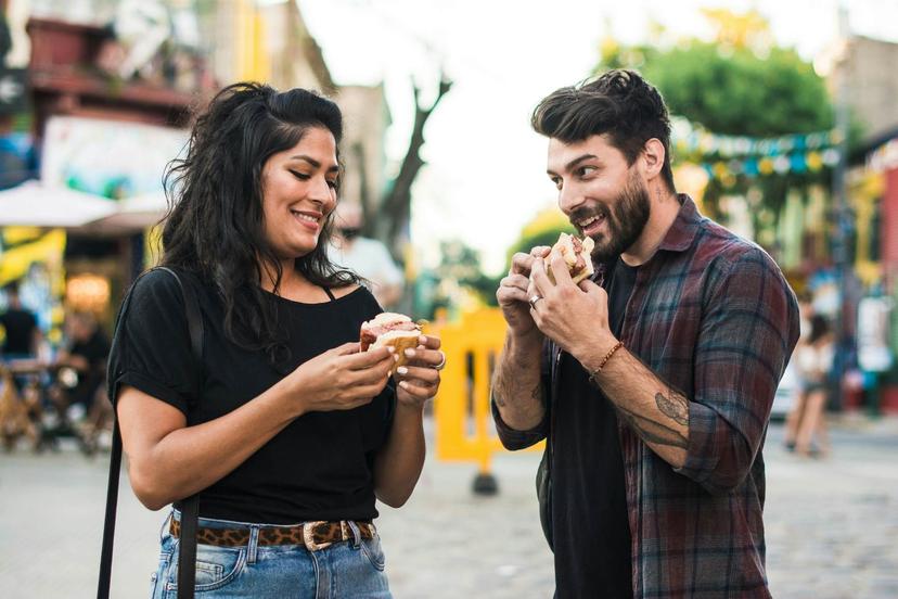 Young couple visiting Buenos Aires and tasting the local street food snack in the street fair: a choripan, which is a grilled chorizo sandwich.

