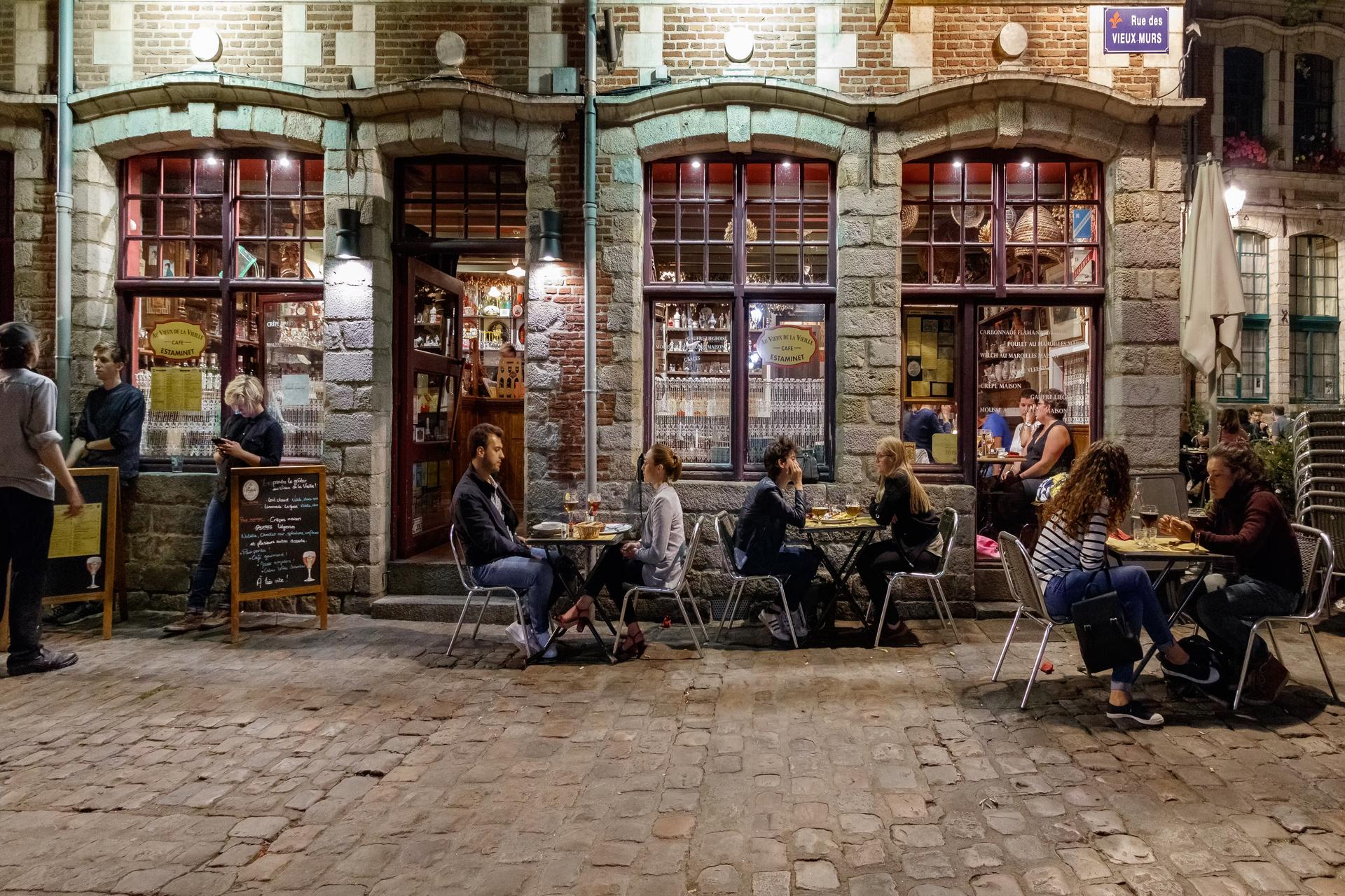 Folk sitter utanför en traditionell fransk bar på kvällen i Lille. 