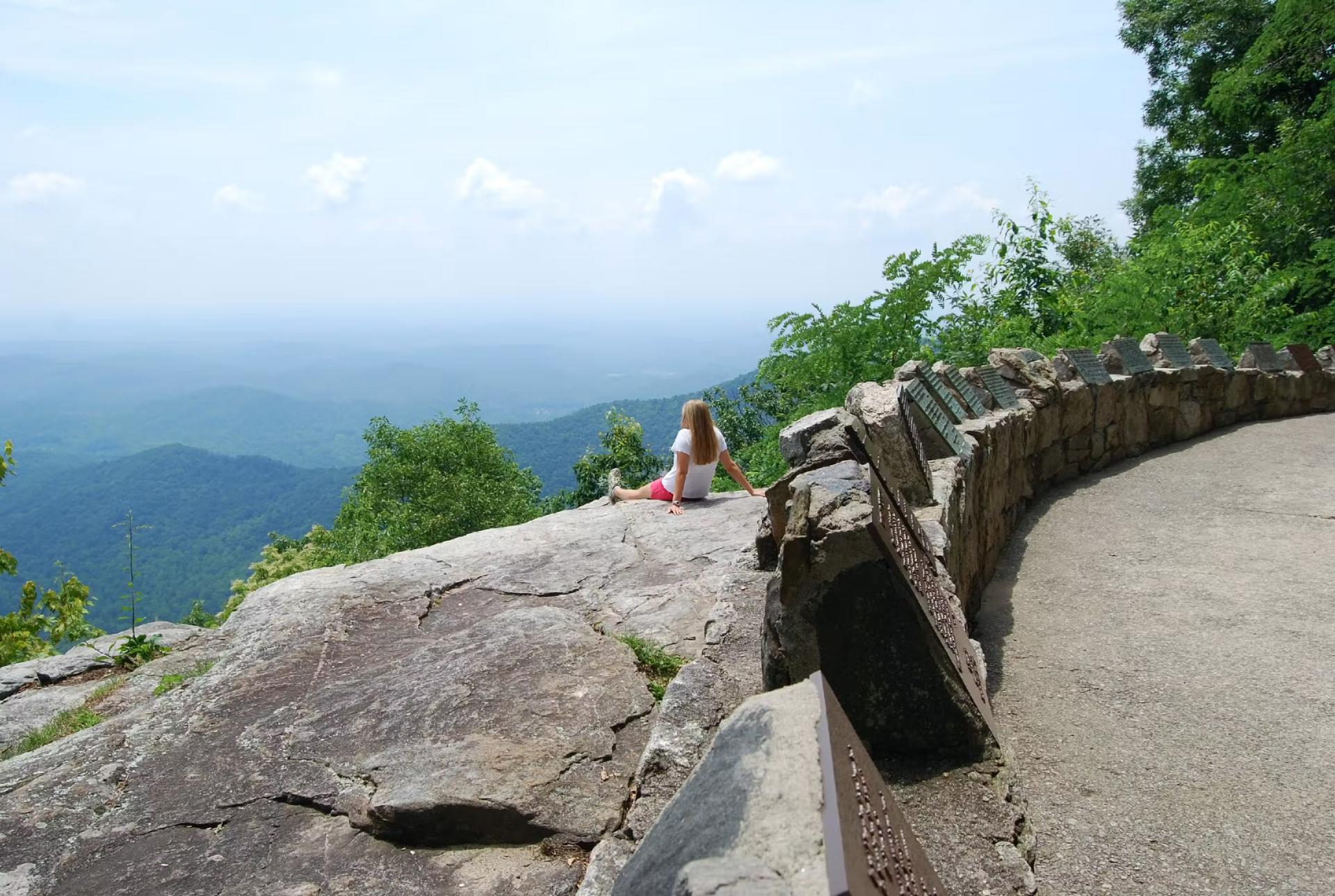 En kvinna som sitter på en klipphäll med en vidsträckt utsikt över Blue Ridge Mountains