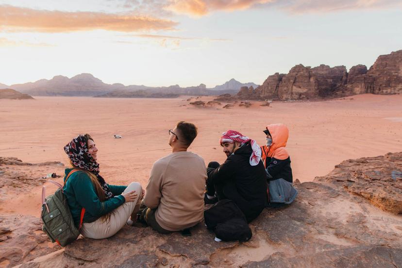 Mixed-race group of females and males having picnic at the edge of the cliff with view of the red sands and majestic mountains in Wadi Rum, Middle East