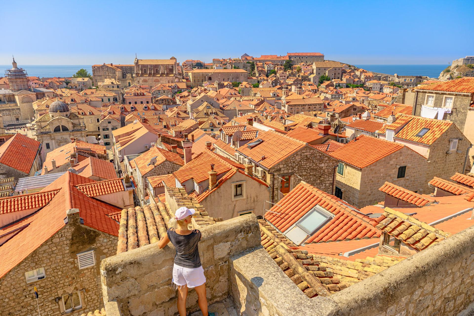A woman stands at a viewpoint along the city walls in Dubrovnik looking out over the many red roofs in the Old Town