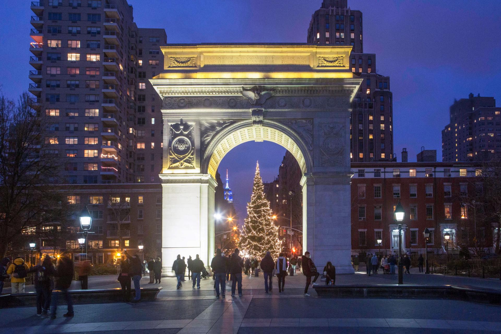 Silhouettes of people standing in front of a fully lit Christmas tree underneath the arch in Washington Square Park 