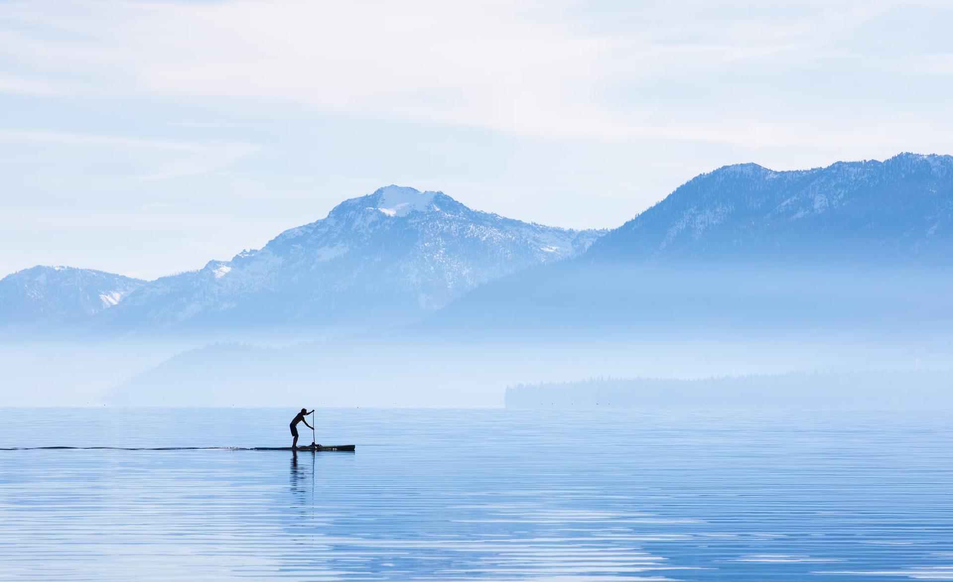 A paddleboarder goes for a morning cruise around the shore of Tahoe City. Lake Tahoe is a high alpine lake located in the Sierra Nevada Mountains, California.