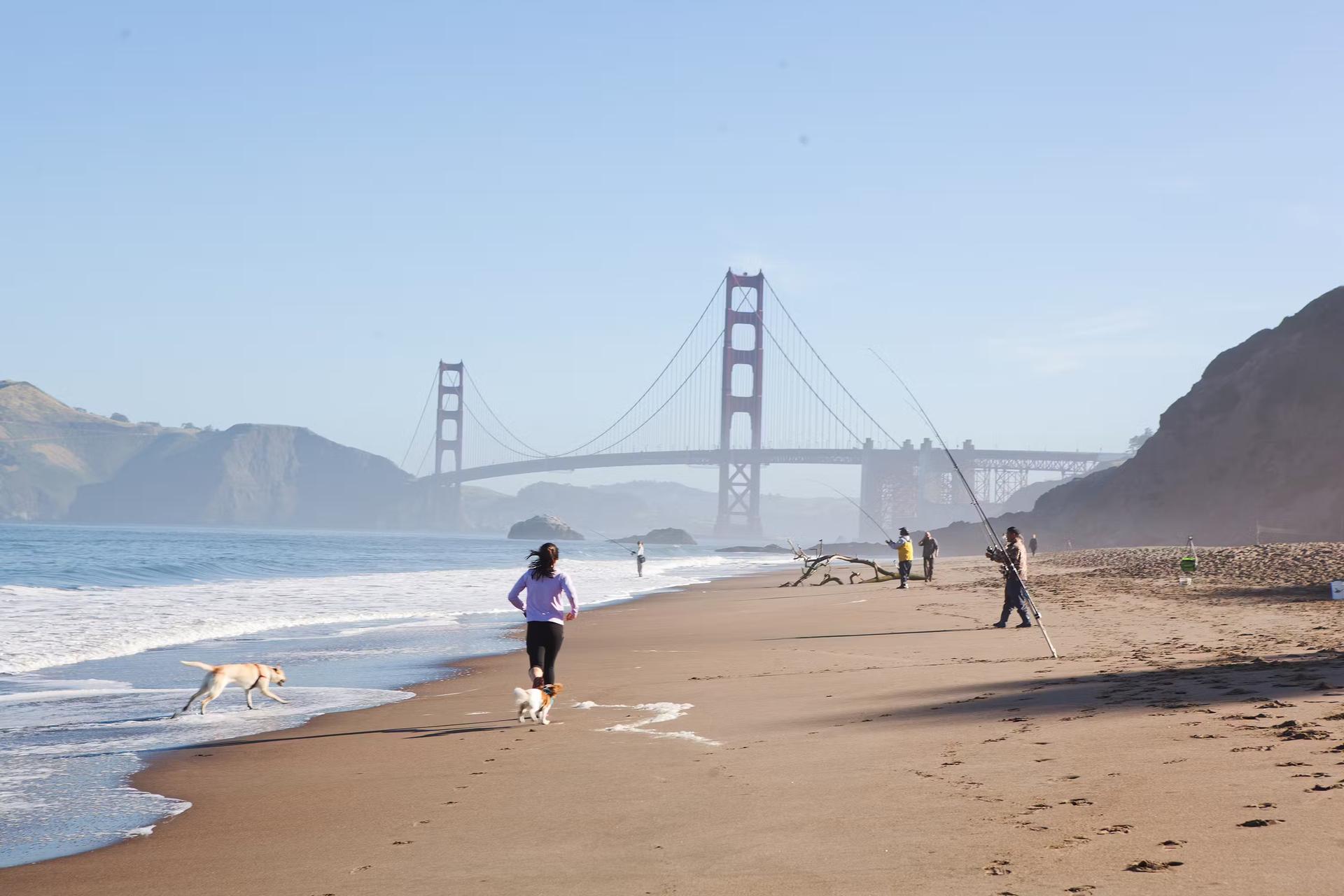 People running and fishing on Baker Beach close to Golden Gate bridge.