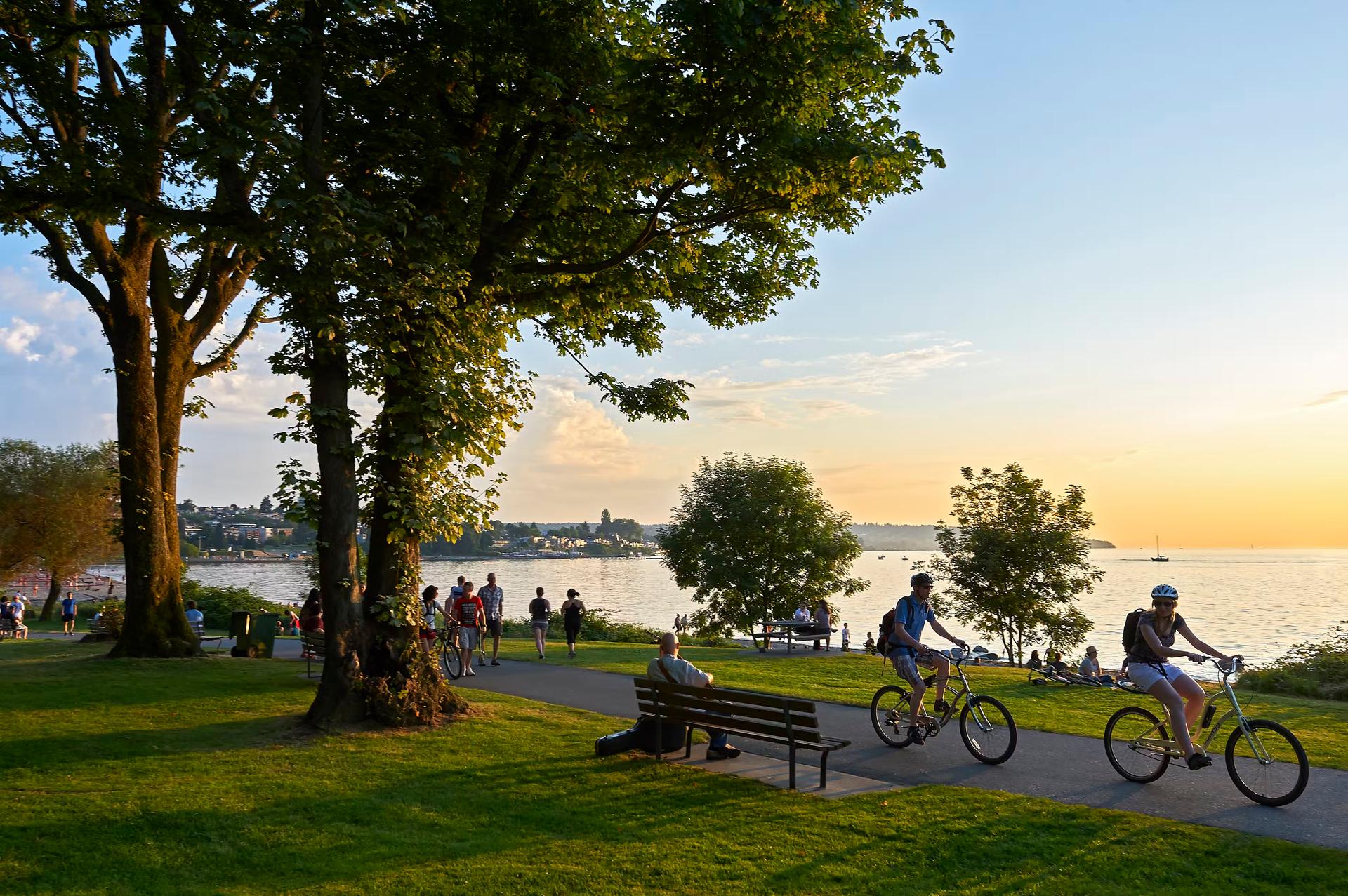 Young couple cycling, others walking or jogging late afternoon and enjoying the sunset at Stanley Park