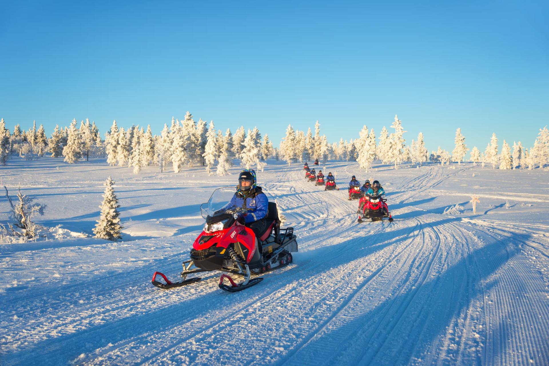 Tourists riding on snowmobiles through snowy conditions in Lapland.