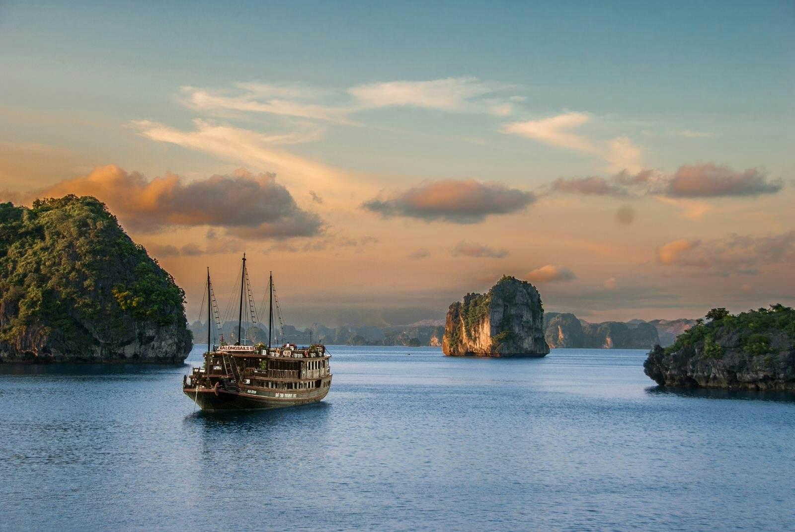 A traditional boat sails on the waters of Halong Bay, with limestone pillars protruding from the water surrounding it
