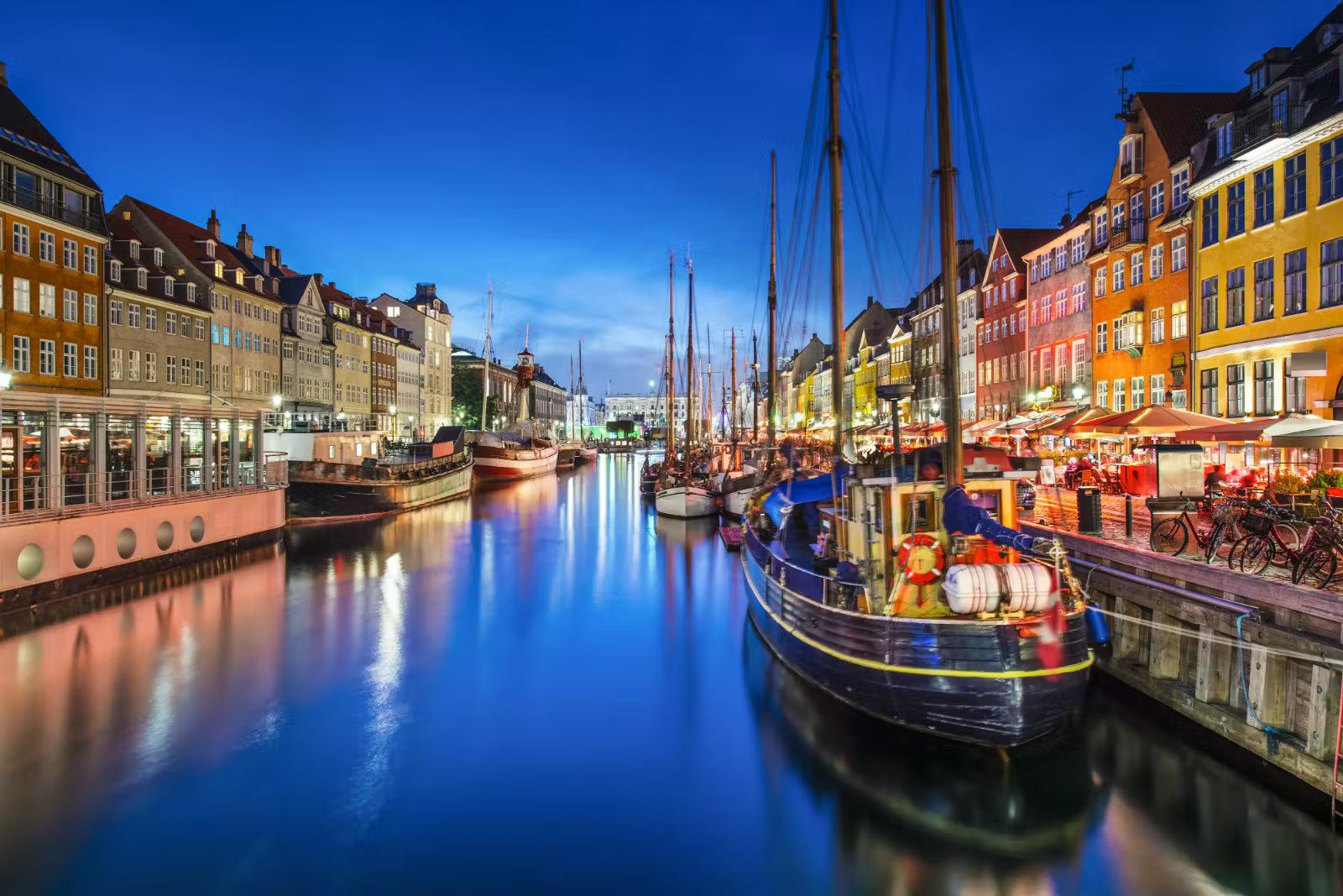 Colourful Nyhavn at night - tall ships and colourful buildings line the river as well as market stalls and parked bicycles