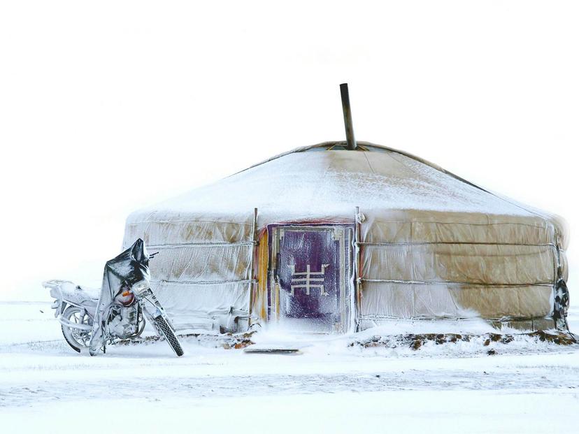A yurt tent with a red door is covered in snow with a motorcycle iced over outside © Chantal de Bruijne / Shutterstock