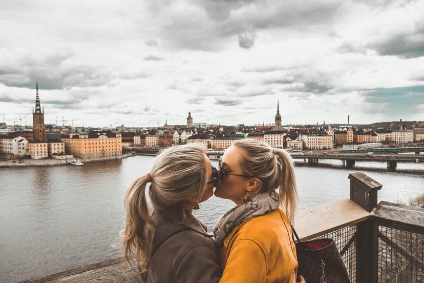 Whitney &amp; Megan kissinhg with view of Stockholm behind them.