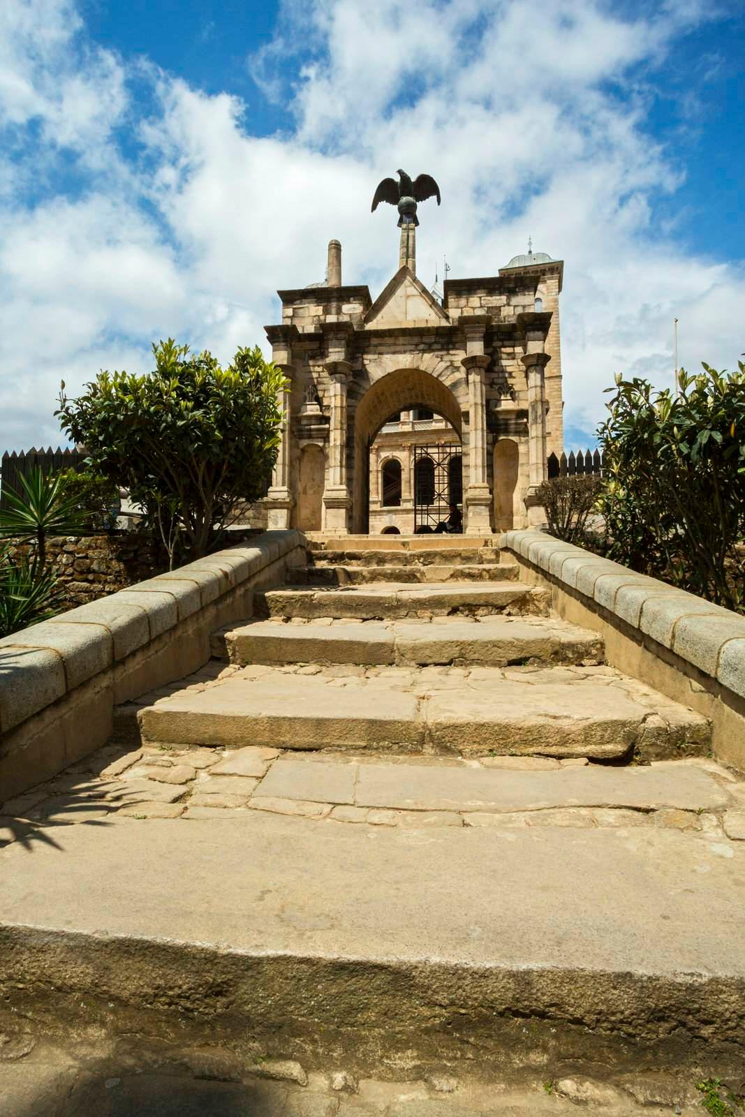 This image looks up a step of wide (and long) stone steps towards an ornate stone gate topped by a copper/bronze eagle statue. The Rova stands in the background © Yann Guichaoua-Photos / Lonely Planet