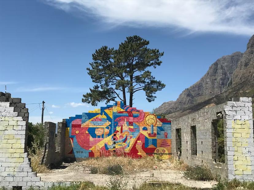 A fantastically bright mural covers one of two remaining stone walls of a ruined home in Kylemore. A large tree climbs into the sky behind it, with the mountains looming in the distance © Simon Richmond / Lonely Planet