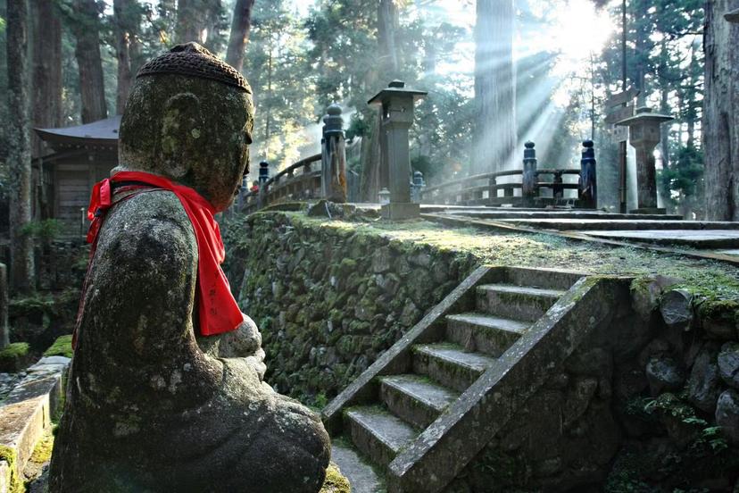 A statue stands in Oku-no-in as dappled sunlight shines through the trees