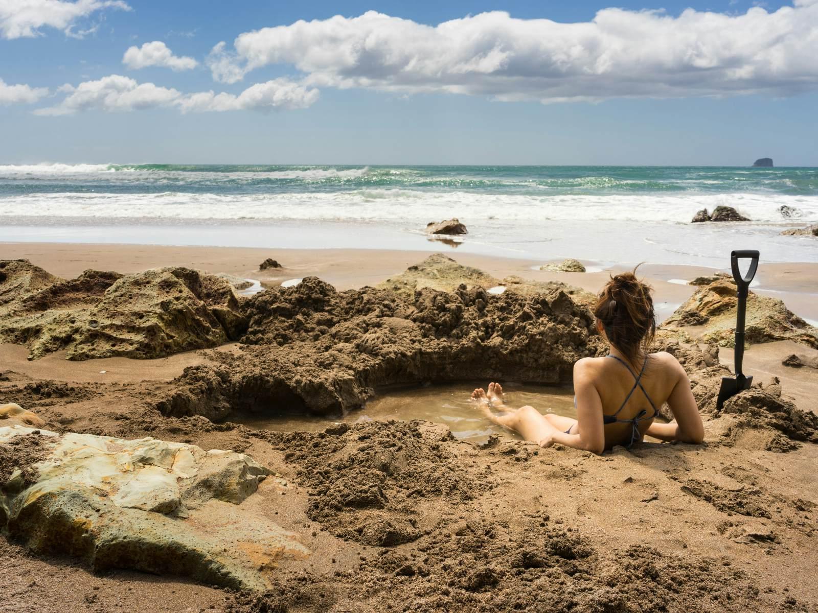 En kvinna som sitter i en självgrävd varm pool på Hot Water Beach, Nya Zeeland