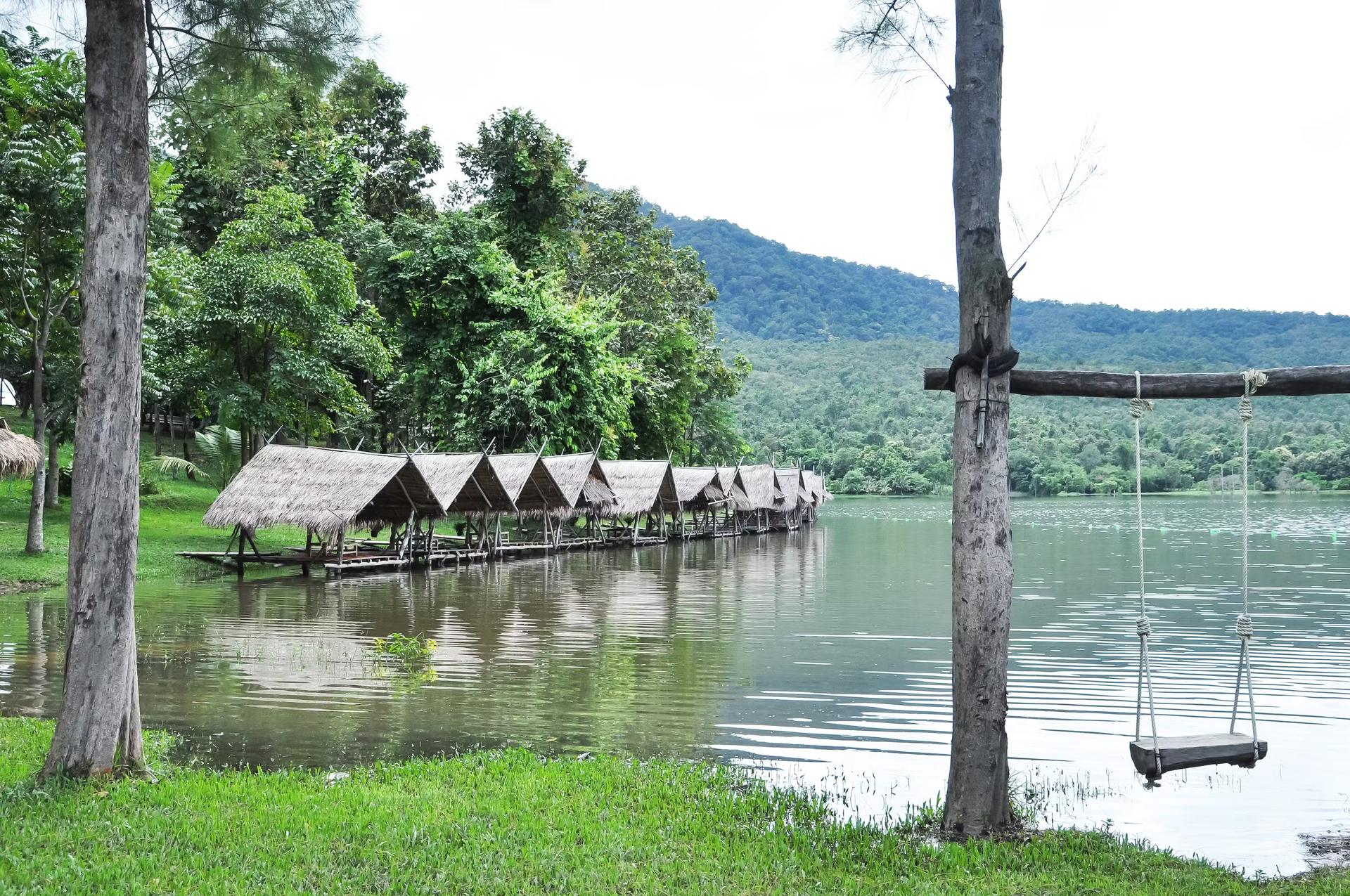 En rad bambuhyddor står vid kanten av Huay Tung Tao, en konstgjord reservoar nära Chiang Mai.  En gunga dinglar från ett träd i förgrunden.