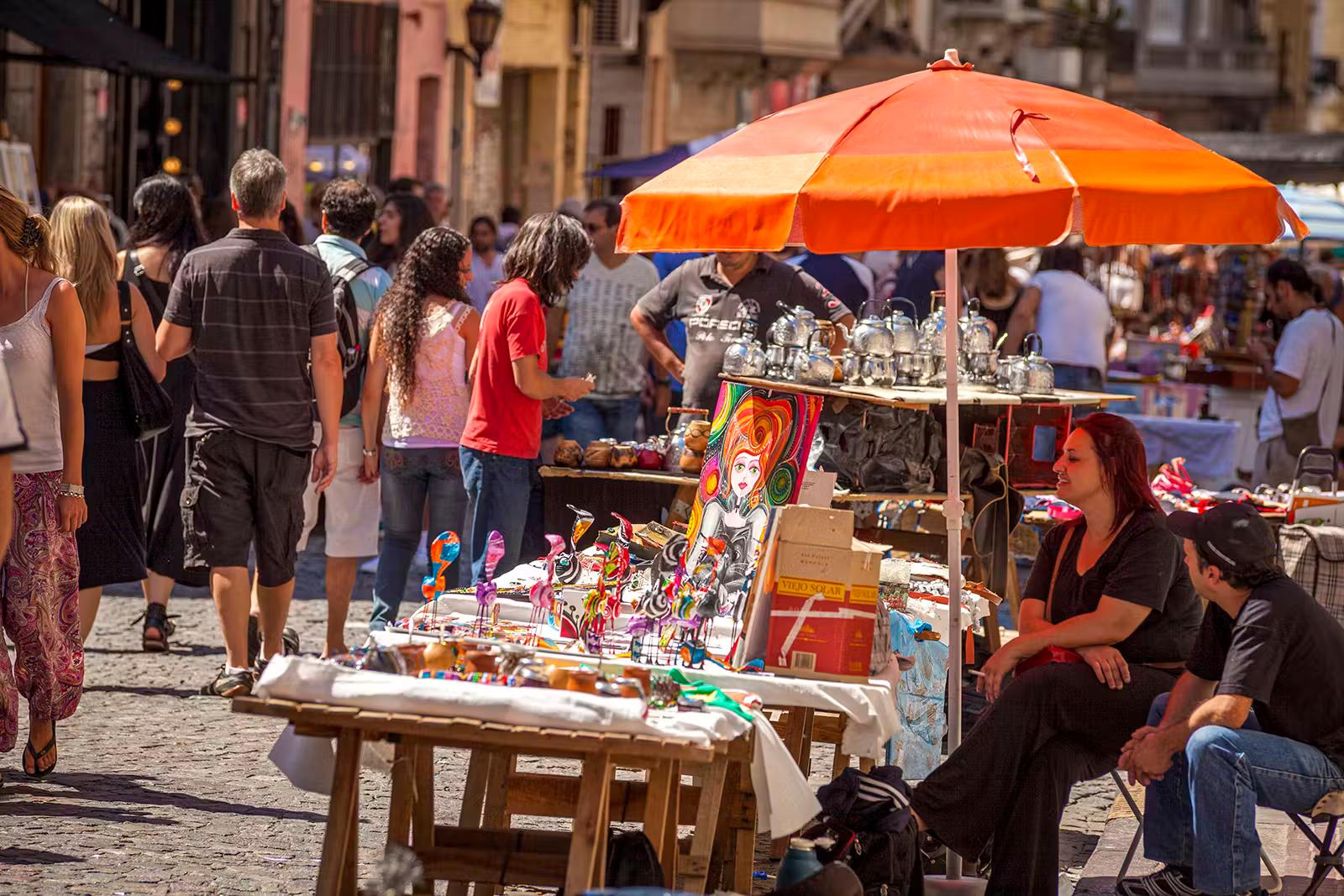 En kvinna sitter under ett orange paraply vid ett konststånd på San Telmo Market, Buenos Aires